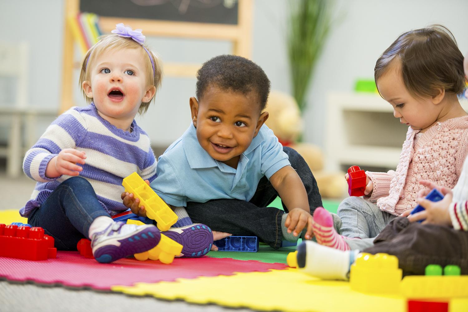 Three toddlers playing with building blocks in nursery