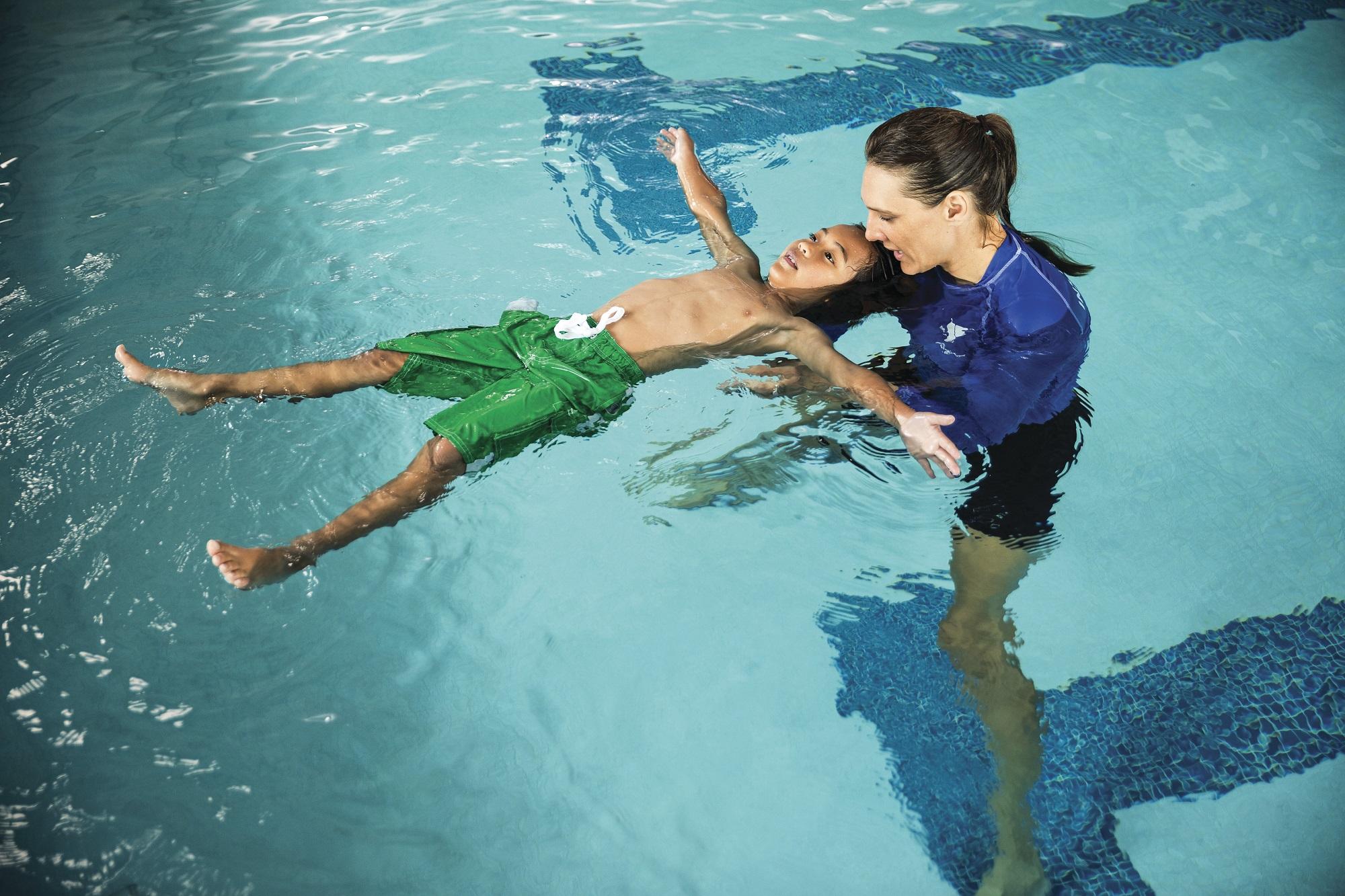 Swim instructor teaching a kid to float on his back.